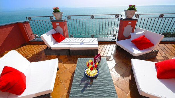 A balcony with white lounge chairs, red cushions, and a decorative table with flowers. - Palazzo Rocco - Penthouse White Moon in Love - 2 rooms - 2 bath - 6 pax max (Praiano)