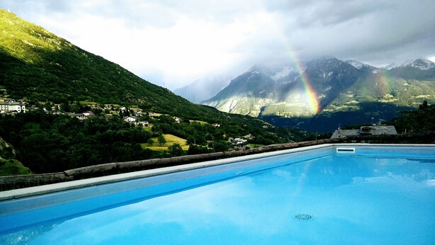 A swimming pool with a view of a mountainous landscape and a rainbow. - Studio With Panoramic View (Gignod)