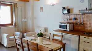 A cozy living room with a wooden dining table, white sofa, and a small kitchen area with a microwave and kettle. - Studio With Panoramic View (Gignod)