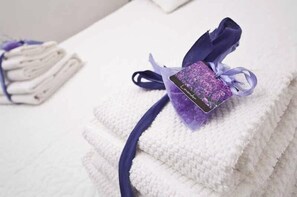 A neatly folded white towel with a purple ribbon and a lavender tag on a white textured surface.