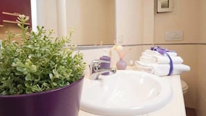 A bathroom with a white sink, a purple potted plant, a mirror, and a towel rack with towels. - Confortevole Appartamento Vicinissimo al Vaticano, Metro, AC & Fast Wifi (Rome)