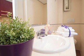 A bathroom with a white sink, a purple potted plant, a mirror, and a towel rack with towels. - Comfortable Apartment Very Close to the Vatican Free Wifi No123 (Rome)
