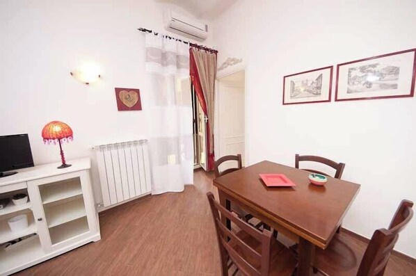 A dining area with a wooden table and chairs, a white cabinet with a television, and a radiator.