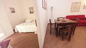 A compact living space with a dining area, a red sofa, and a bed with a white cover. - Confortevole Appartamento Vicinissimo al Vaticano, Metro, AC & Fast Wifi (Rome)