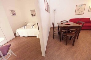 A compact living space with a dining area, a red sofa, and a bed with a white cover.