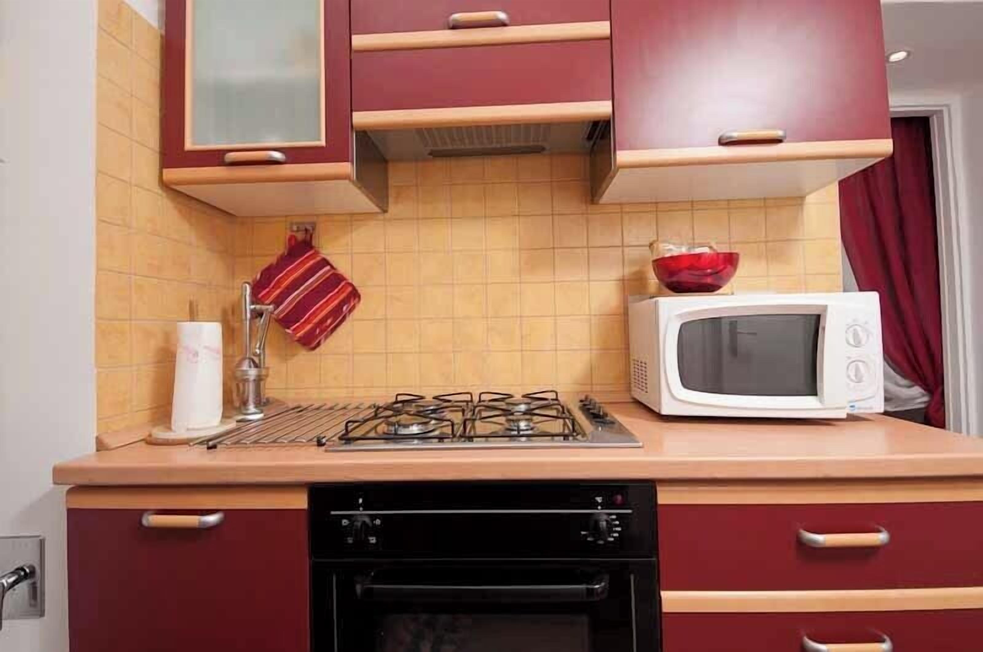 Una cocina con estufa a gas, microondas, escurreplatos y una toalla roja colgada en la pared.