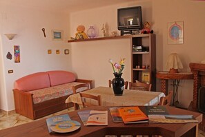 Un salon confortable avec un canapé, une table à manger ornée de livres, un vase rempli de fleurs et un téléviseur.