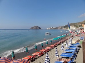 A beach with rows of sun loungers and umbrellas, a clear sky, and a distant island. - Villa La Favola Suite Ischia Terrace With View (Barano d'Ischia)