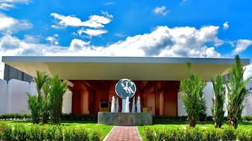 Un edificio moderno con una gran fuente central, rodeado de exuberante vegetación y palmeras.
