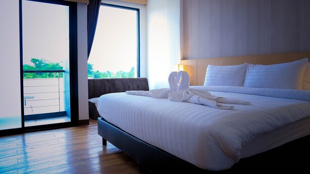 A hotel room with a large bed, a sliding glass door to a balcony, and a view of greenery outside.