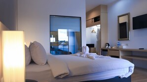 A modern hotel room with a large bed, a desk, a mirror, and a view of the outdoors.