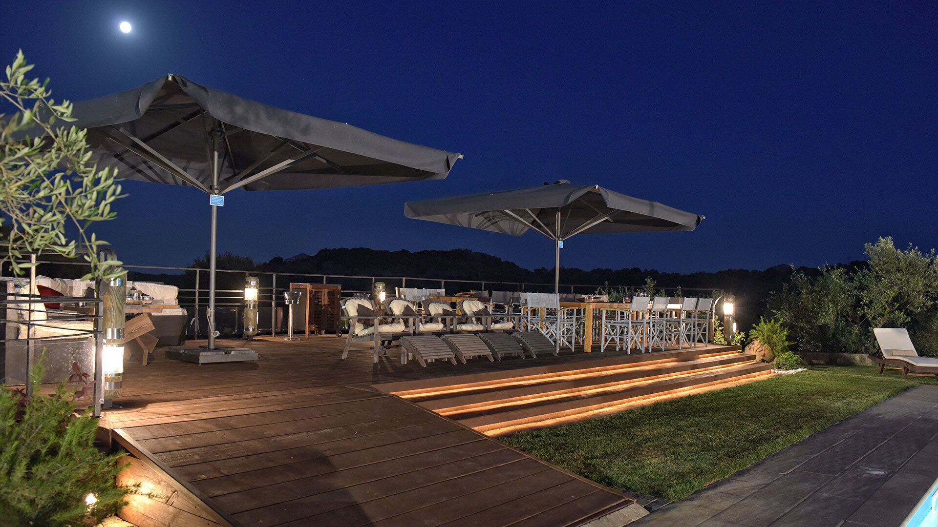 An outdoor deck with wooden flooring, multiple lounge chairs, and umbrellas.
