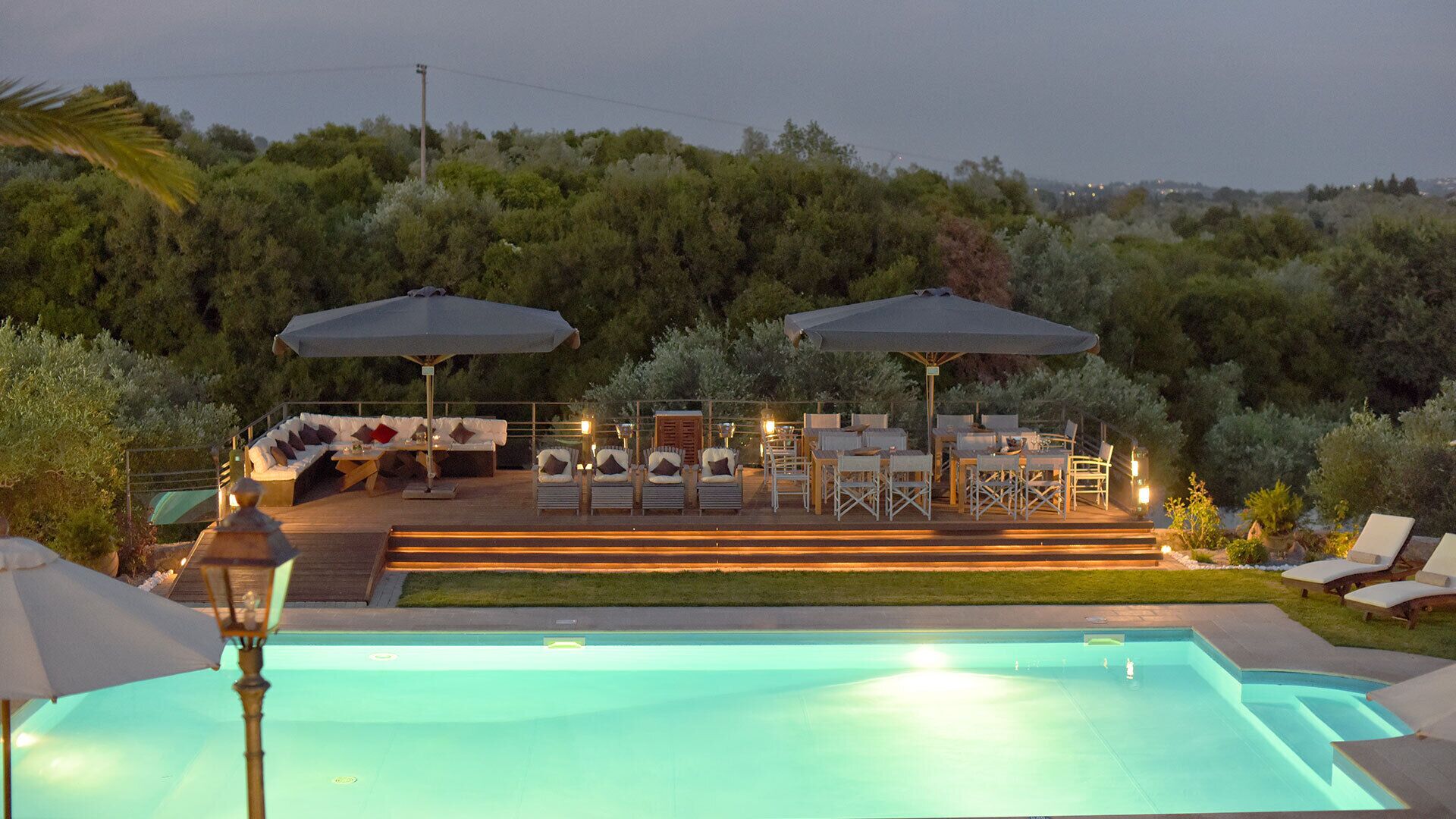 A swimming pool with lounge chairs and umbrellas, surrounded by greenery.
