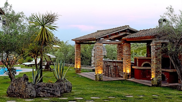 A patio area with a brick barbecue, stone pillars, and a pergola.