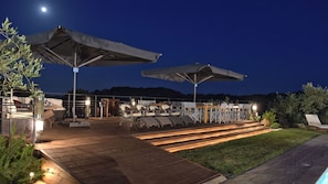 Relax in the evening with a view of the surrounding landscape from this outdoor seating area featuring comfortable tables and chairs under shade.