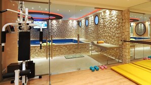 Ein Fitnessraum mit Trainingsgeräten, einer Massageliege und einer Steinwand.