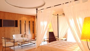 Ein Schlafzimmer mit Bett, Nachttisch, Sessel, Wandfernseher und Holzschrank.
