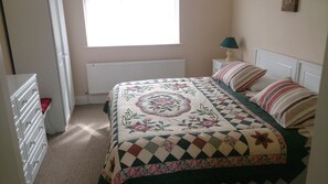 Une chambre à coucher comprenant un lit, une commode, une fenêtre, un radiateur et une table de chevet avec une lampe.