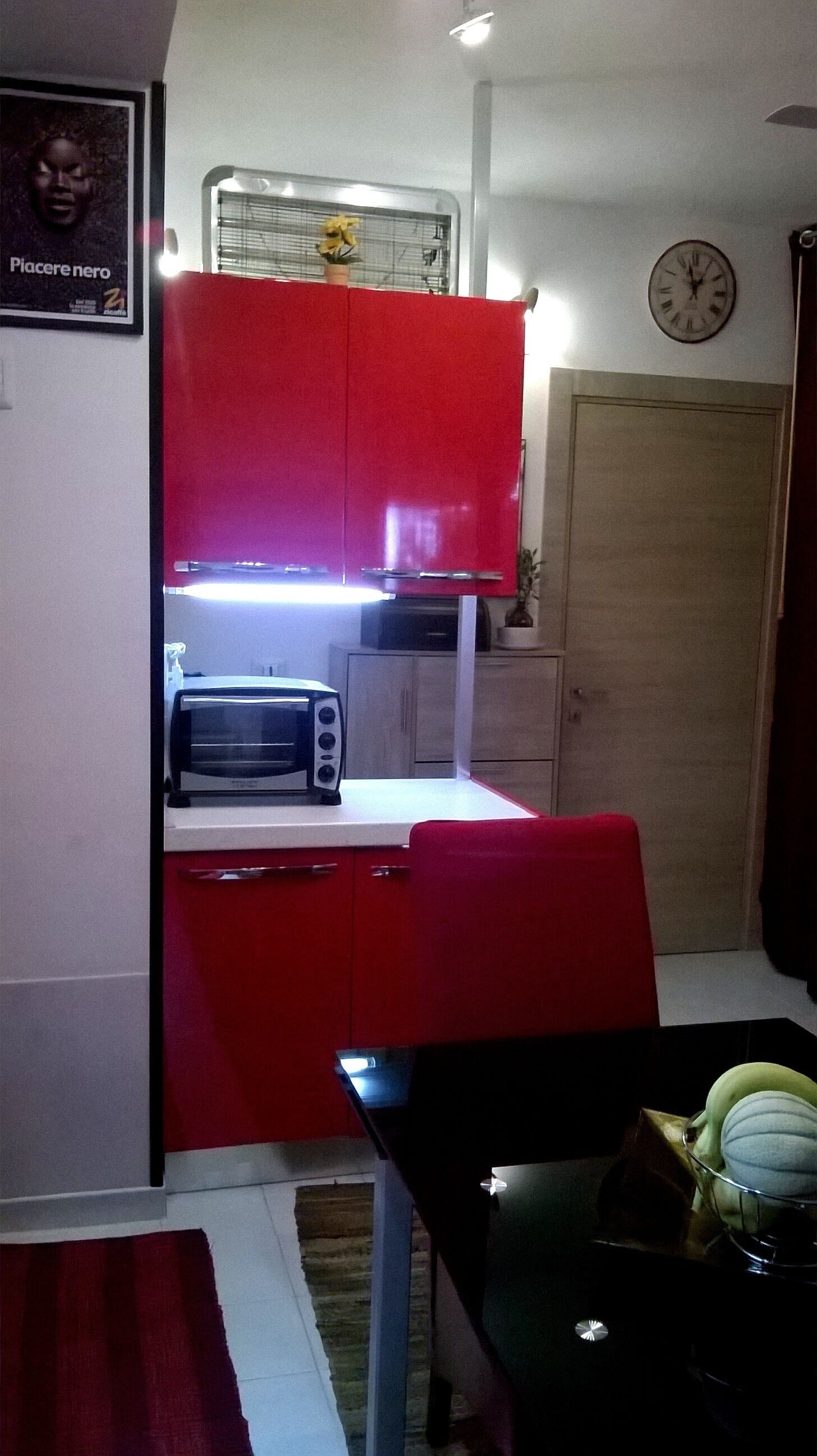 Una cucina compatta con mobili rossi, un forno a microonde e una sveglia appesa al muro.
