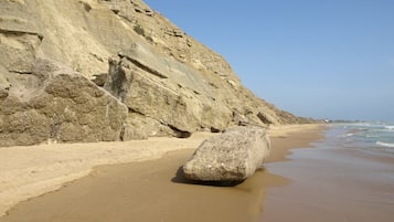 A beach with a large rock in the foreground and a rocky cliff in the background.