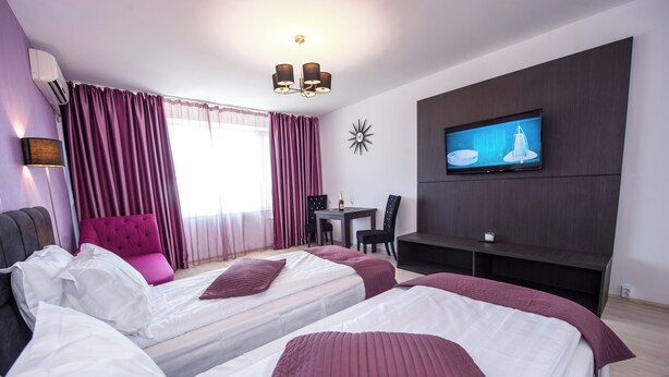 Hotellihuone, jossa on kaksi sänkyä, televisio, ruokapöytä ja tuoli.