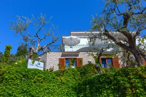 A building with a stone facade, red shutters, and a white umbrella. - Villa Marianna Like Paradise in Amalfi Coast!!! (Massa Lubrense)