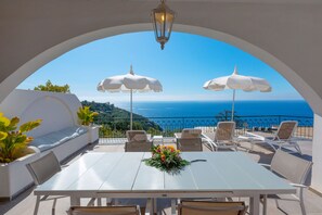 A terrace with a table, chairs, and umbrellas, overlooking a scenic view of the sea and hills. - Villa Marianna Like Paradise in Amalfi Coast!!! (Massa Lubrense)