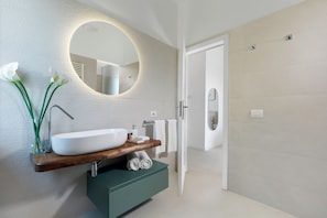 A modern bathroom with a large oval mirror, a wooden vanity, a white sink, and a built-in shower.