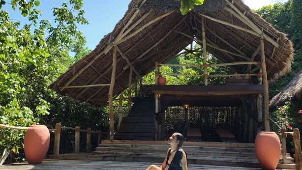A person sitting by a pool with a thatched-roof structure in the background. - Fundu Lagoon (Pemba Island)