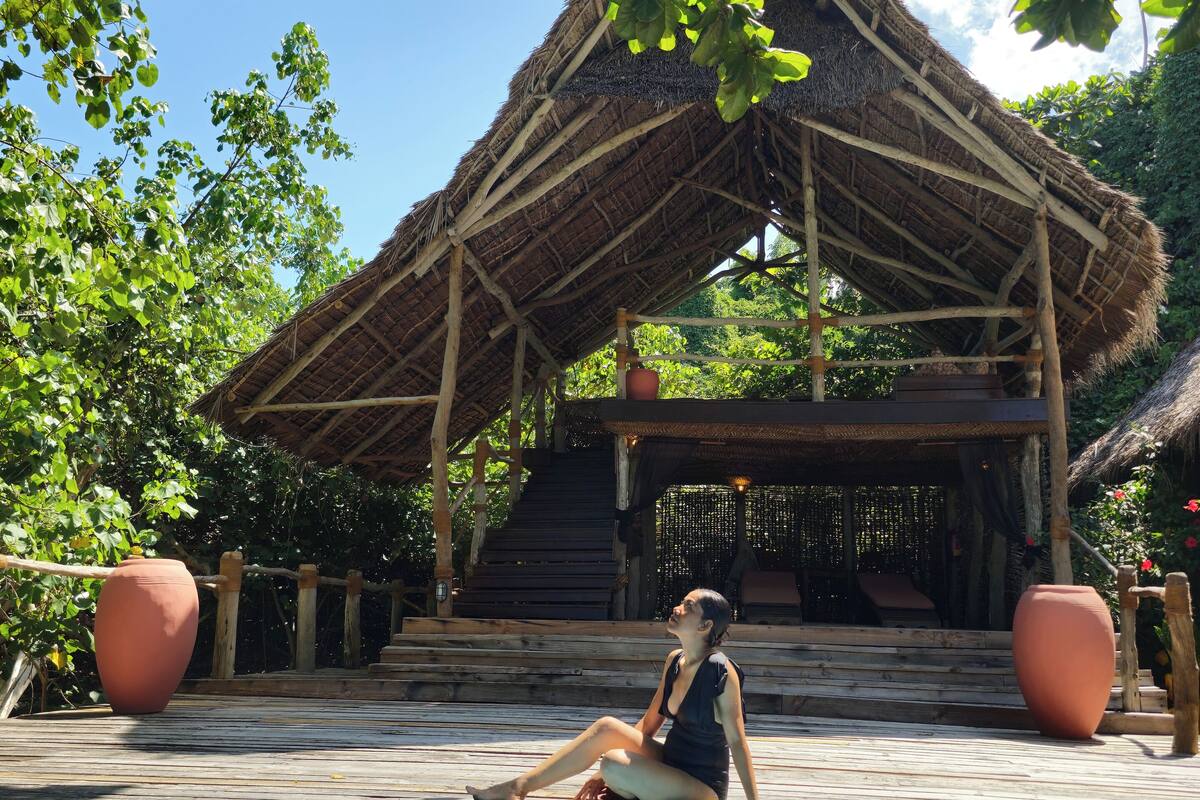 A person sitting by a pool with a thatched-roof structure in the background.