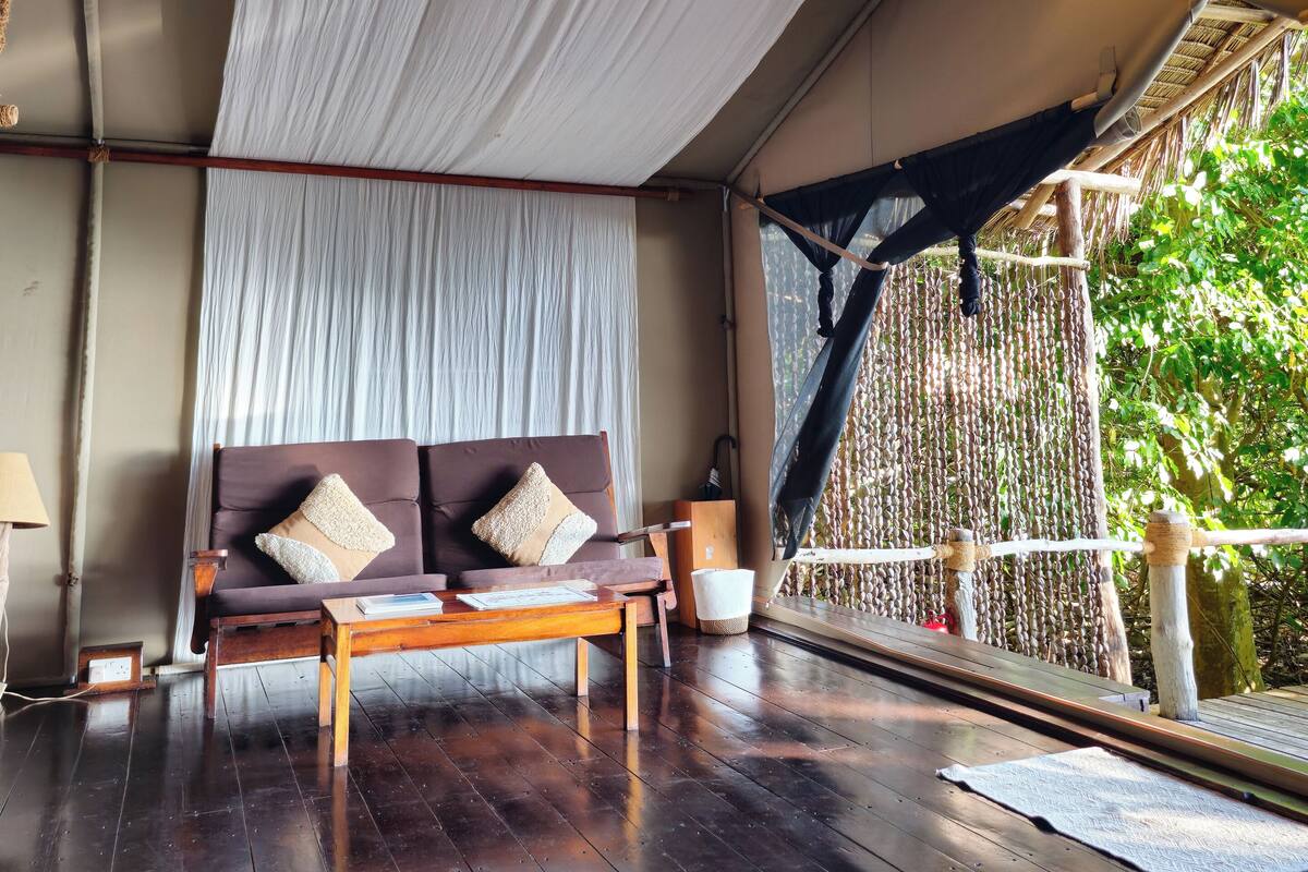 A room with a wooden floor, a sofa with cushions, a ceiling fan, and a hanging light fixture.