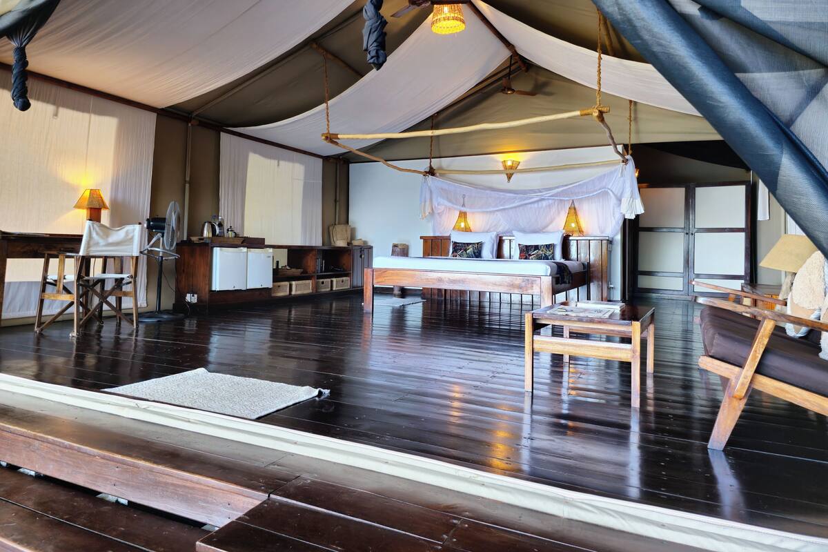 A tented accommodation with a wooden floor, a bed, a desk, and a chair.