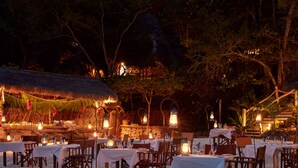 An outdoor dining area with tables and chairs, surrounded by trees and a thatched-roof structure. - Fundu Lagoon (Pemba Island)