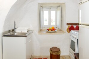 A compact kitchen with a sink, stove, and a small window with a fruit bowl on the windowsill.
