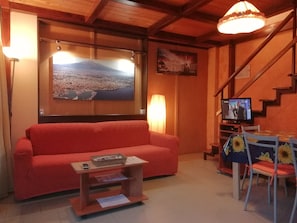 A cozy living room with a red sofa, a wooden coffee table, a TV on a stand, and a staircase.