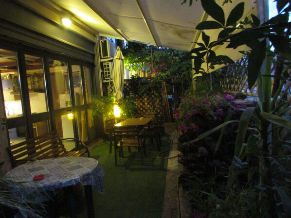 An outdoor patio area with a table and chairs, surrounded by plants and a fence.