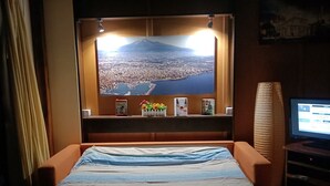 A hotel room with a bed, a large window with a cityscape view, a television, and a small table with a vase of flowers. - House Between Etna and the sea Near Taormina (Santa Venerina)