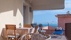 A balcony with a table, chairs, and a lounge chair. - Apartment Rentals Sicily (Avola)