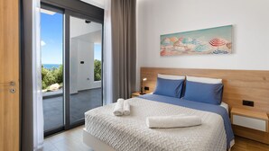 Une chambre moderne avec un grand lit, un tableau représentant des parasols de plage et une vue à travers la porte vitrée.