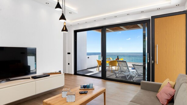 Un salon moderne avec un téléviseur, une table basse en bois et un balcon offrant une vue sur la mer.