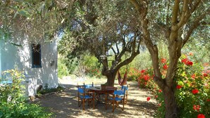 A garden with a table and chairs, surrounded by trees and flowering plants. - Beautiful Country Home on Syros Island, Greece (Syros)