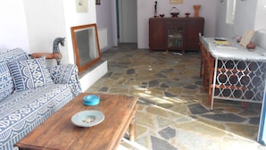 A living room with a patterned sofa, a wooden coffee table, a stone-tiled floor, a cabinet with glass doors, and a striped table. - Beautiful Country Home on Syros Island, Greece (Syros)