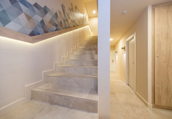 Una escalera con un diseño geométrico en la pared, una puerta de madera y un pasillo con una lámpara.