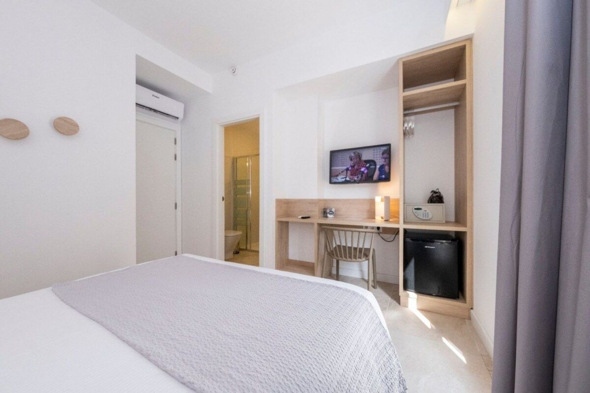 Una habitación de hotel con cama, escritorio con silla, televisor y armario.