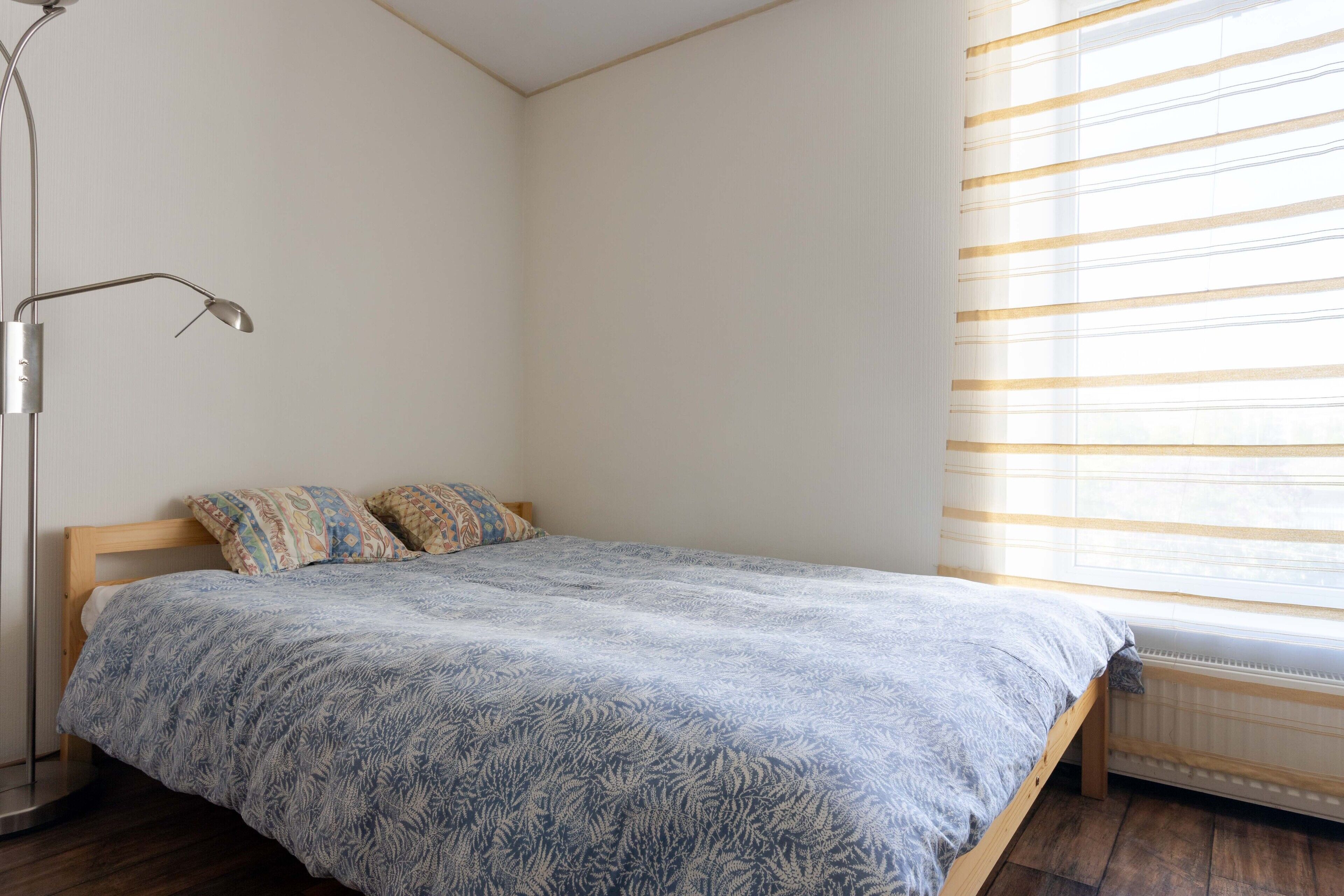 A bedroom with a bed, a radiator, and a window with blinds.