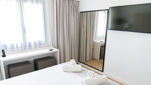 Una habitación de hotel con cama, escritorio, teléfono, espejo y televisión.