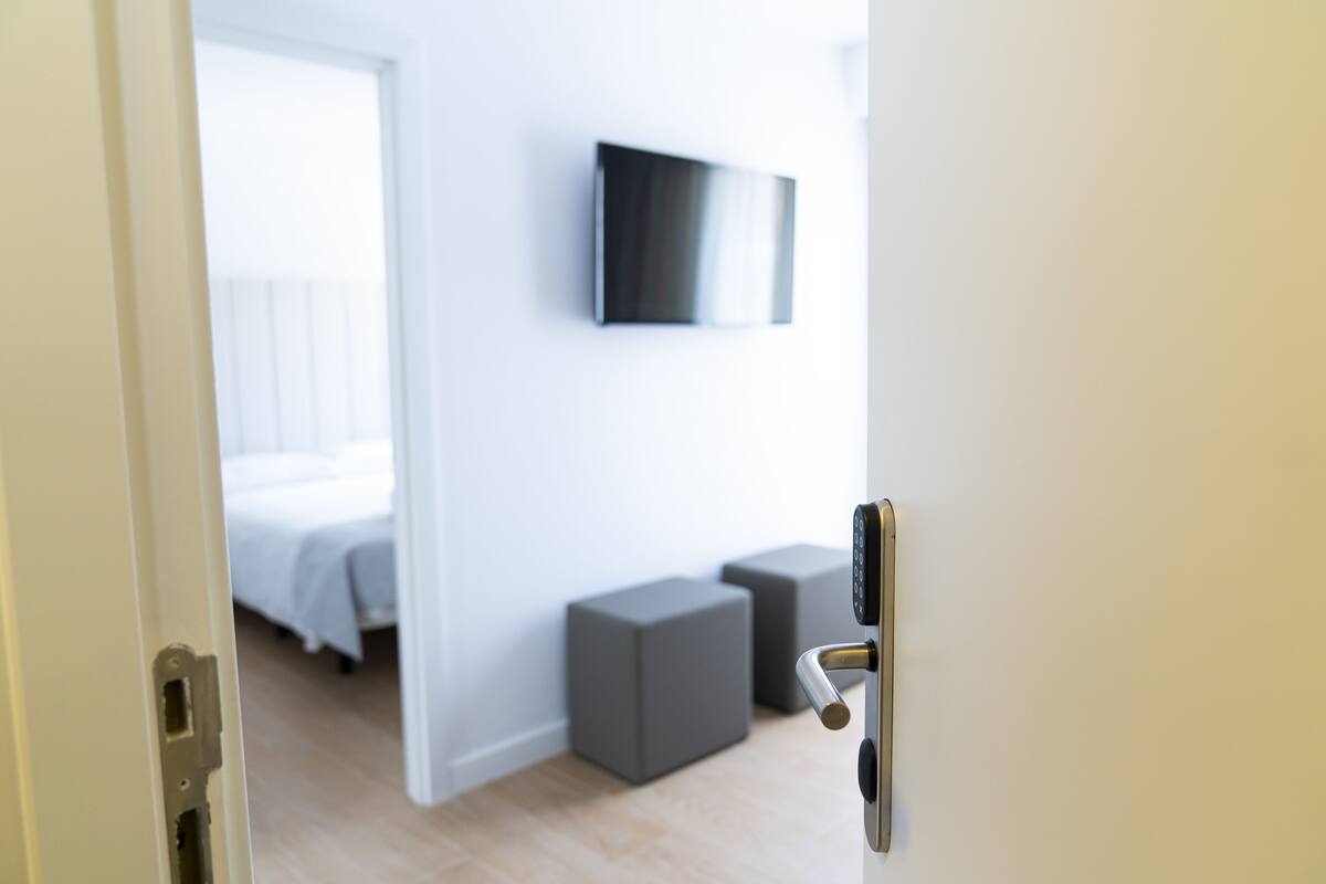 Een moderne hotelkamer met een bed, een flatscreen televisie aan de muur en twee grijze opbergkubussen.