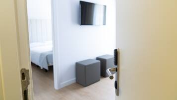 Una habitación de hotel moderna con una cama, un televisor de pantalla plana en la pared y dos cubos grises para guardar objetos.