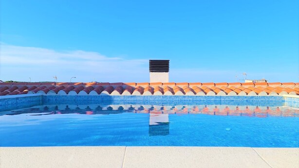 Una piscina con un borde de baldosas y un cielo azul despejado.