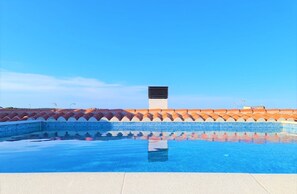 Una piscina con un borde de baldosas y un cielo azul despejado.